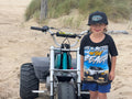 Child wearing black Showoff UTV Life Is Better On The Beach kids tee beside a mini bike in the dunes